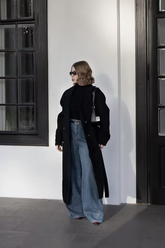 a lady in a black top, a black long wool coat and a pair of blue jeans